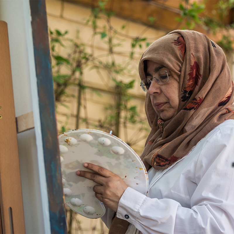 Portrait of Siddiqa Juma award winning islamic artist painting with a palette in hand on a canvas outdoors